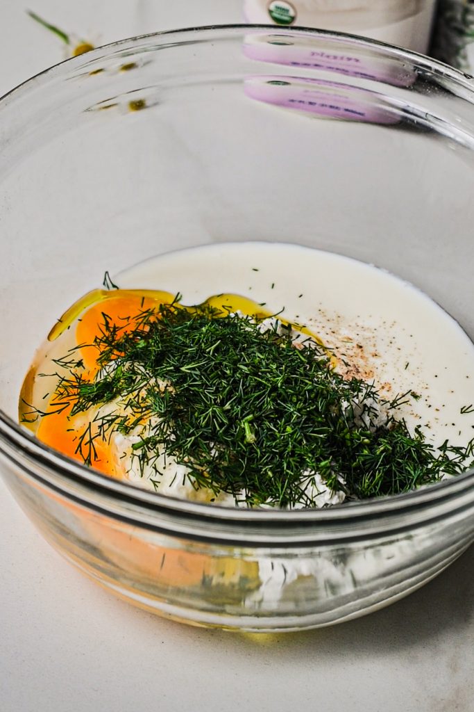 Adding freshly chopped dill into the filling in a glass mixing bowl.