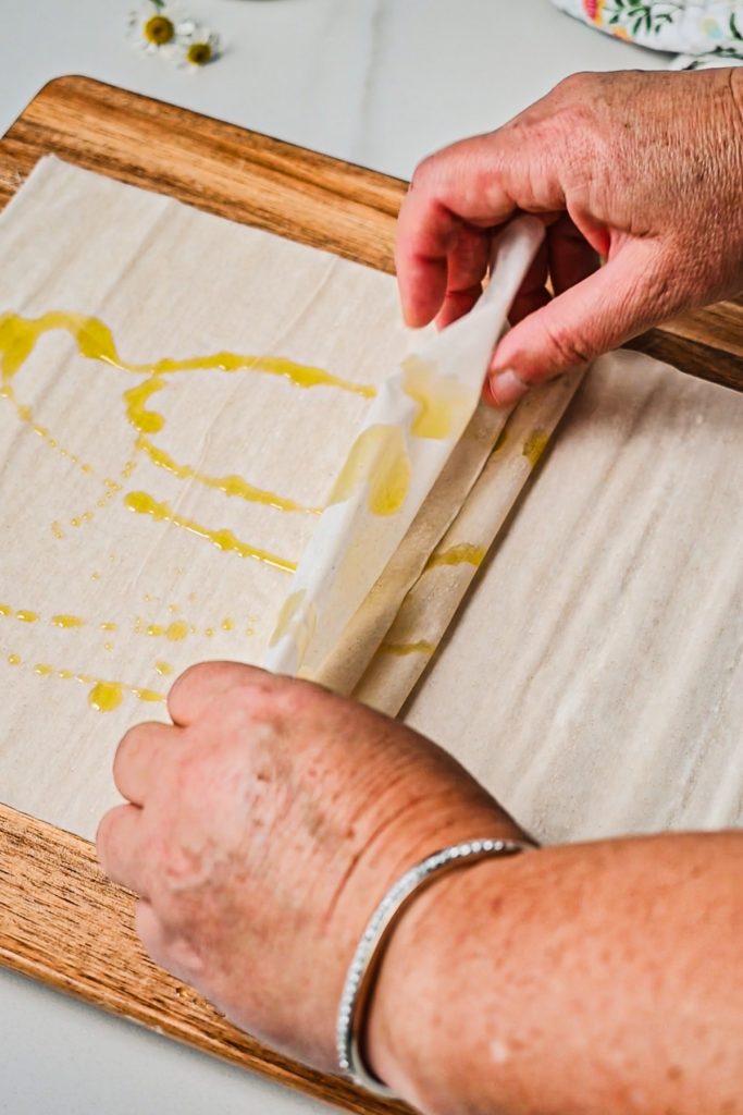 Hands scrunching together the phyllo sheets with olive oil drizzled on them.