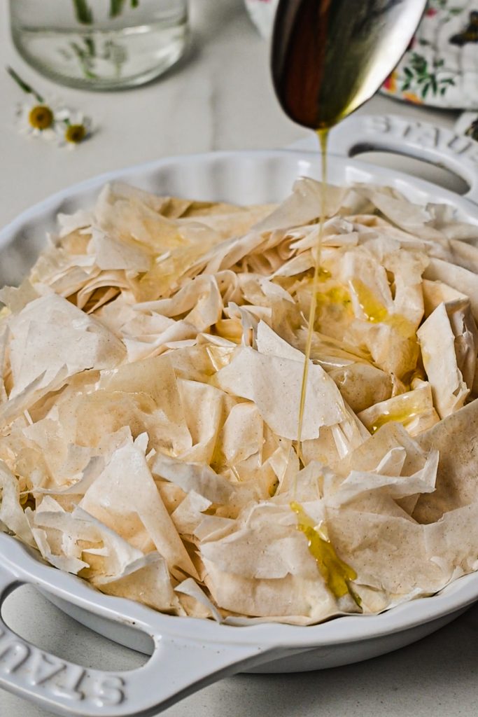Drizzling some olive oil on top of the phyllo pie before baking.