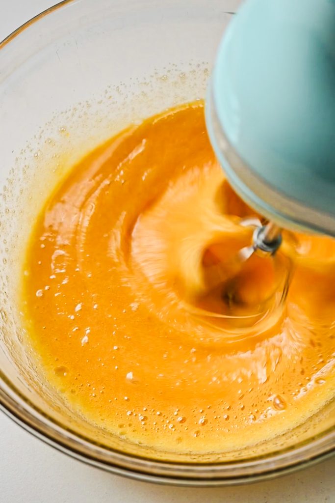 Using an electric hand mixer to combine the lemon sugar with the eggs in a bowl.
