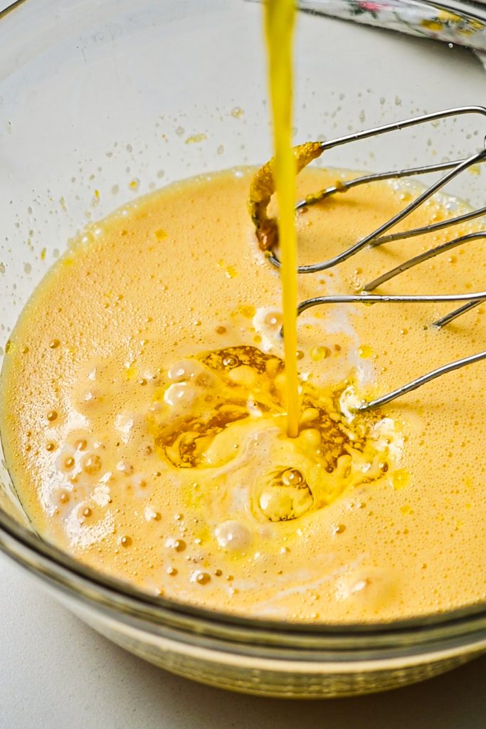 Melted butter being poured into the cake batter in a bowl.