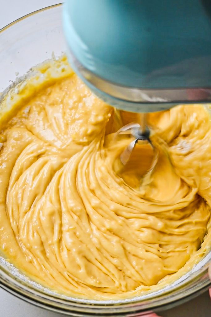 Cake batter in a glass bowl being mixed with an electric hand mixer.