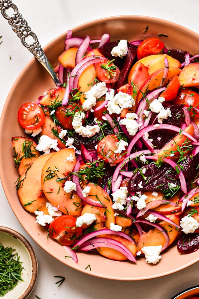 Close up of a peach and beet salad with feta in a salad bowl with a spoon.