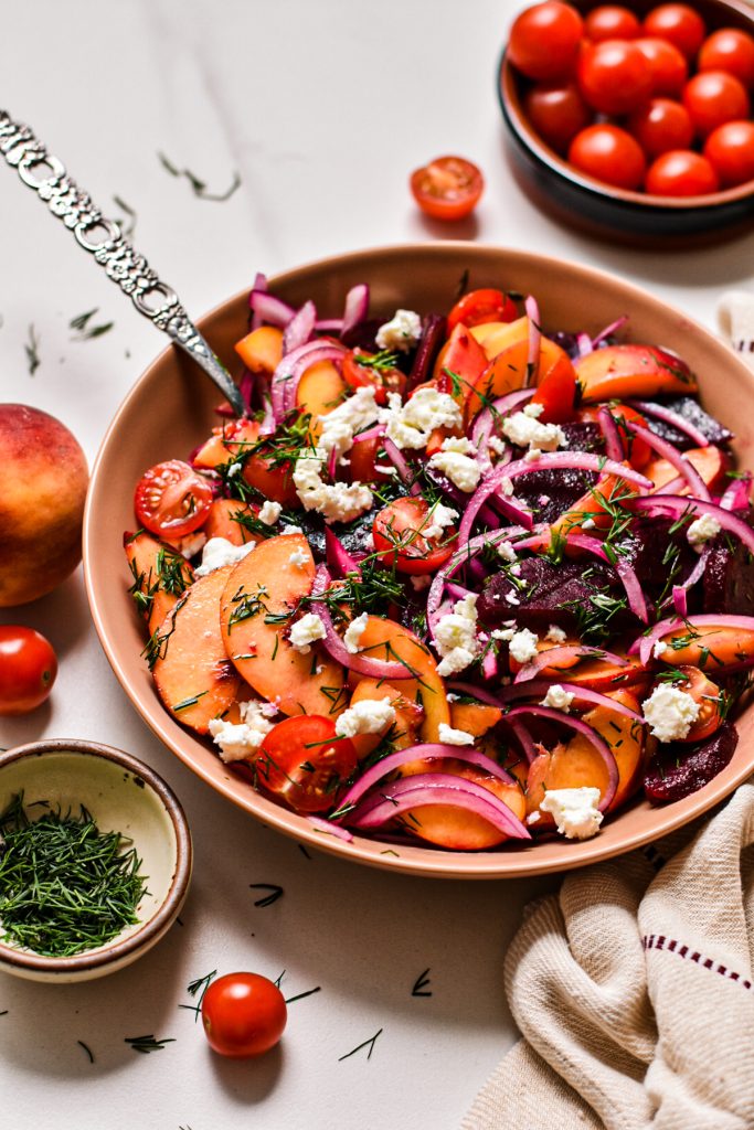 Side view of a peach and beet salad with feta and dill on top.