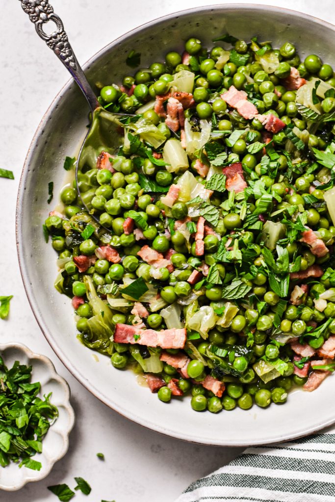 Close up of Peas à la Française (French style peas) in a bowl garnished with fresh herbs.