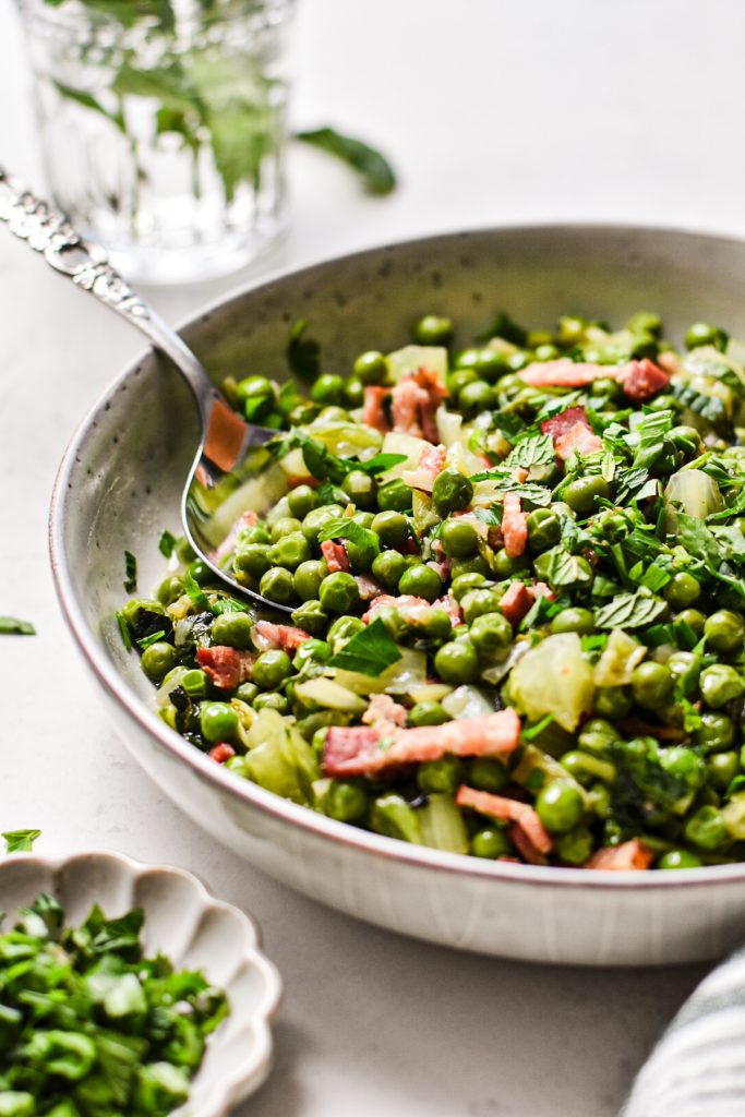 Side view of a shallow bowl served with French-style peas with a spoon in the bowl.