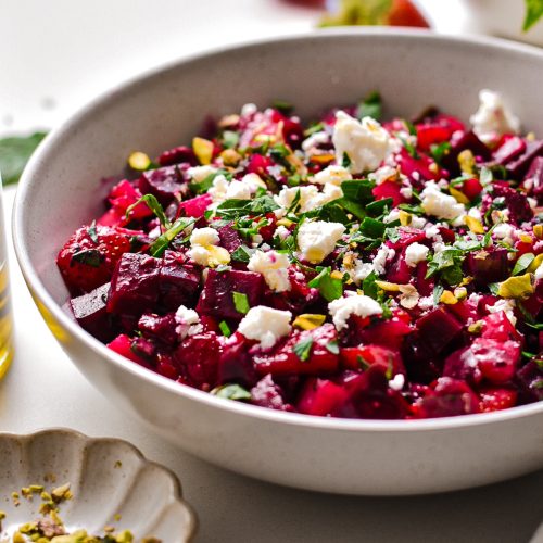 Side view of beet strawberry salad topped with feta and pistachios.