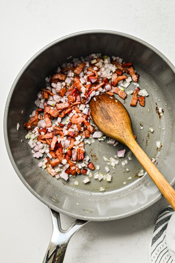 Shallot added to the crisp chopped bacon in a skillet.