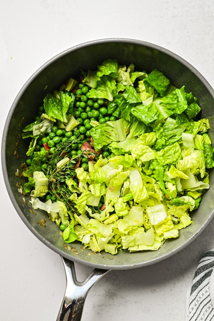 Chopped romaine lettuce and thyme sprigs added to the peas in a skillet.