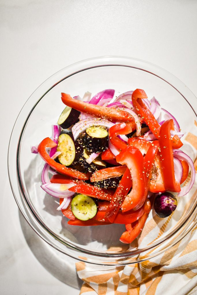 Sliced vegetables in a glass mixing bowl with seasonings.