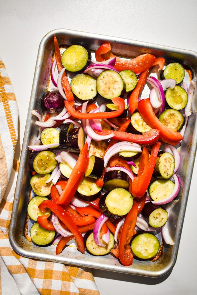 Seasoned vegetables on a sheet pan before being roasted.