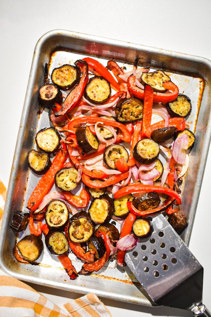 Roasted vegetables on a sheet pan with a spatula.