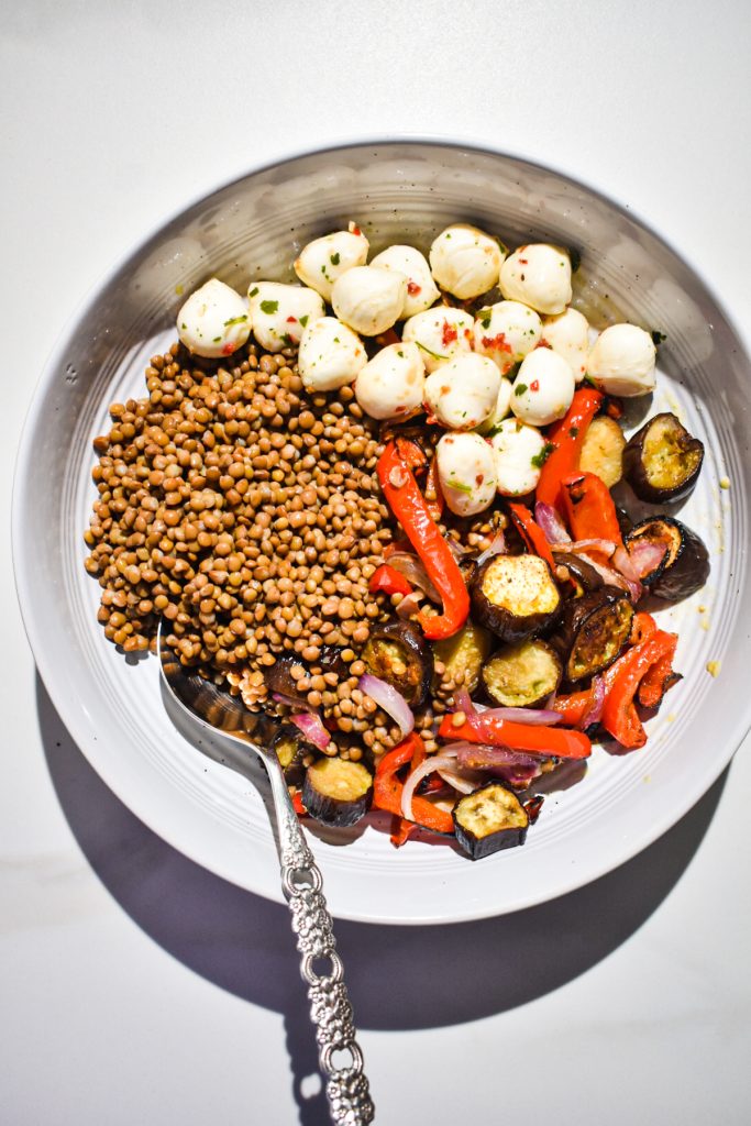Roasted vegetables with cooked lentils and marinated mozzarella balls in a bowl.