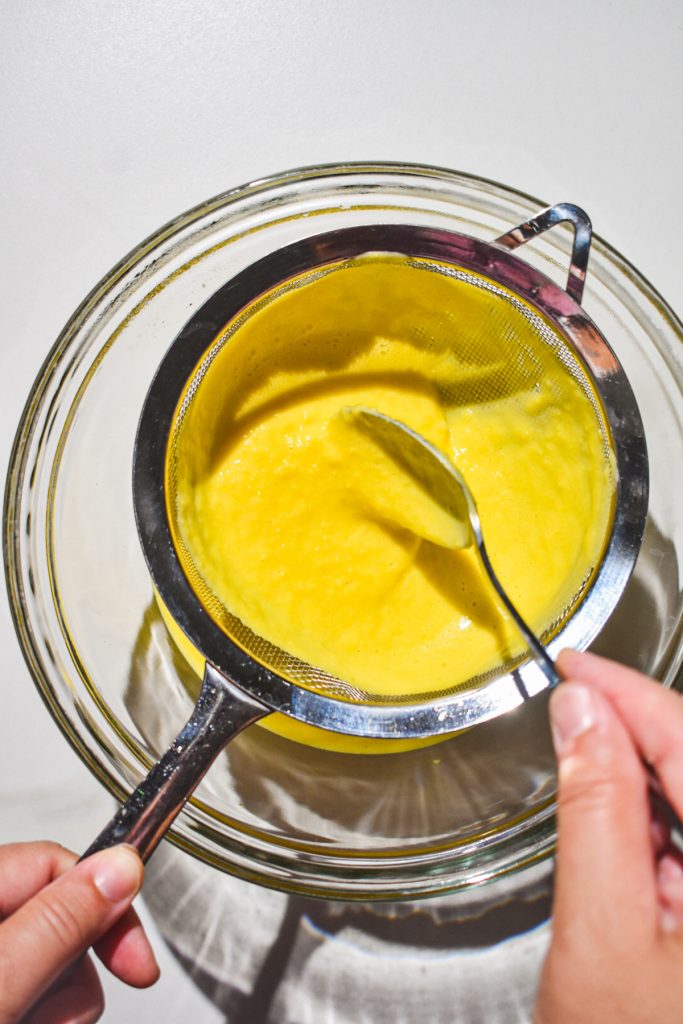 Straining the blended sweet corn through a fine mesh sieve.