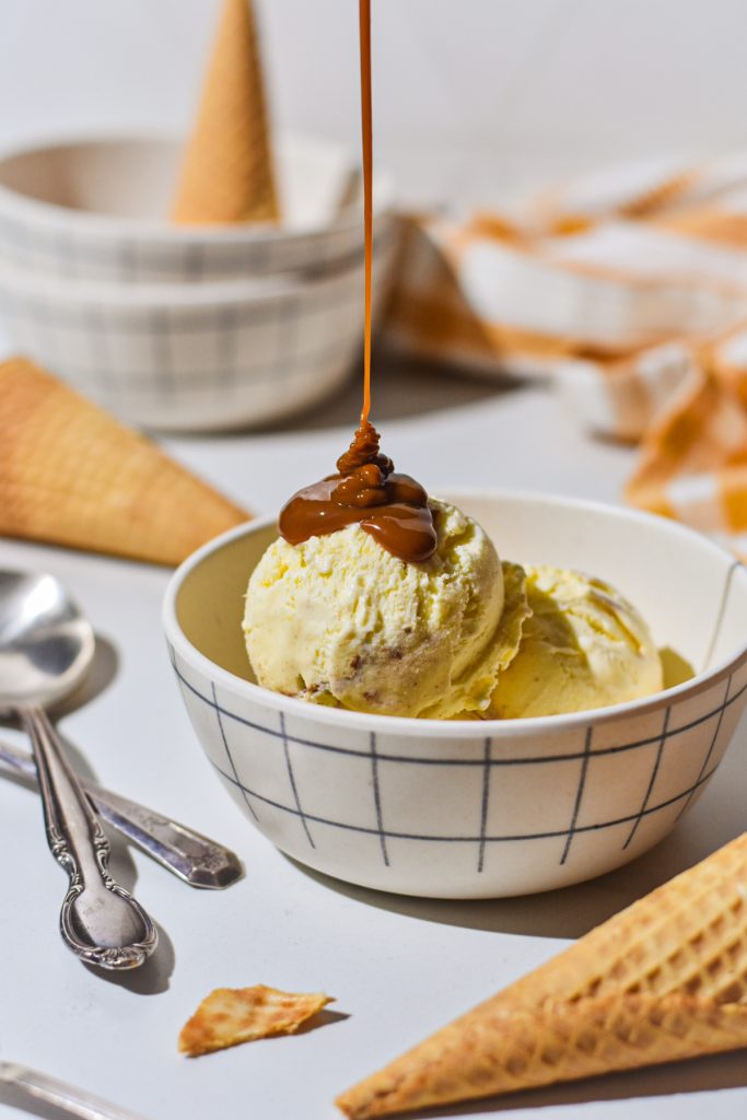Caramel sauce being drizzled onto scoops of sweet corn ice cream in a bowl.