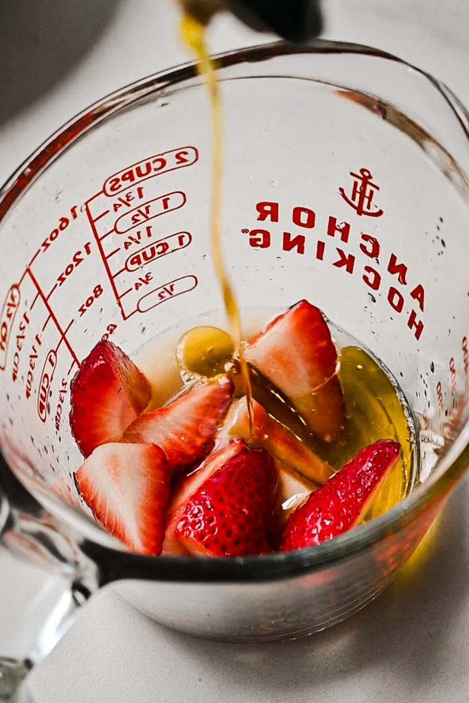 Strawberries in a glass measuring cup with olive oil being poured in.