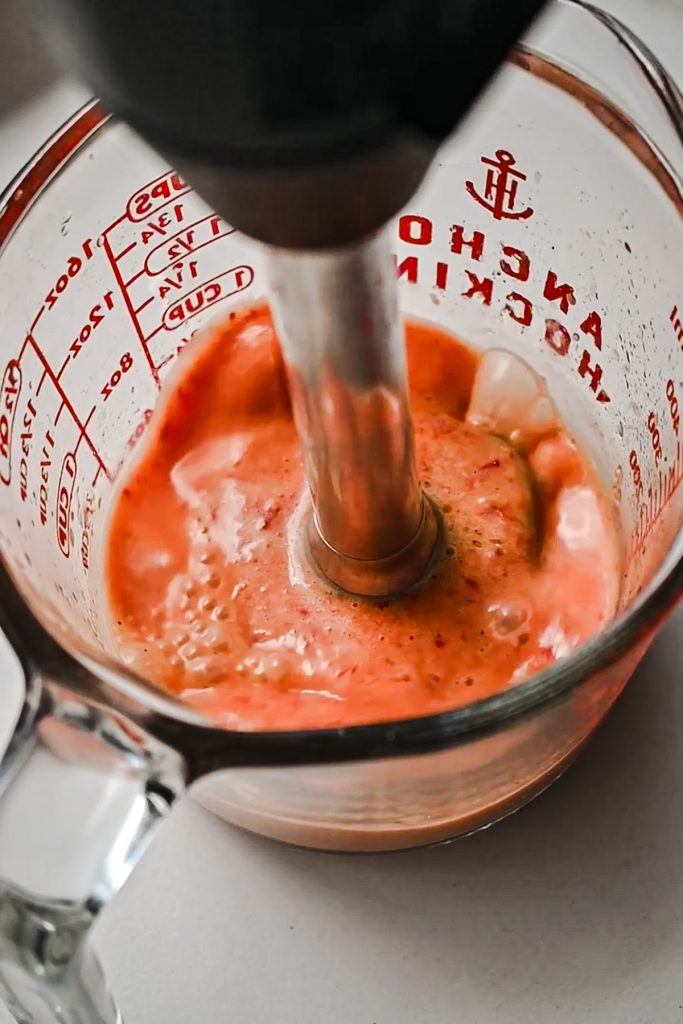 Using an immersion blender to blend together the strawberry dressing.