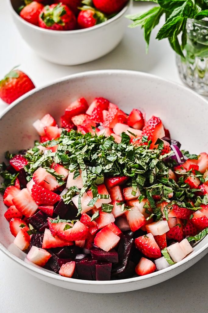 Diced strawberries and chopped herbs added to the bowl of beets.