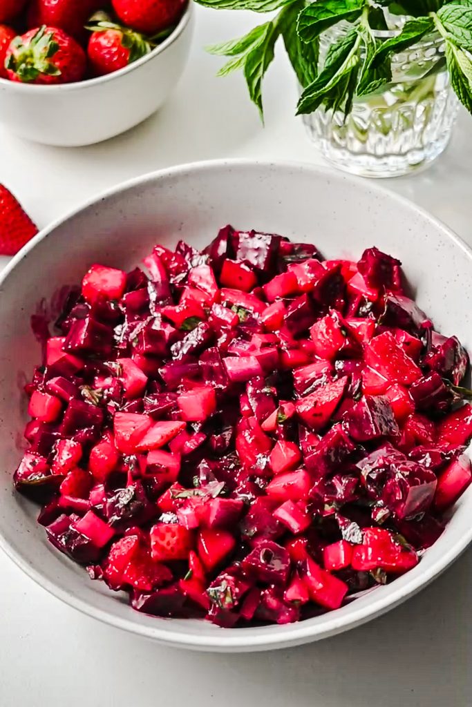 Beet strawberry salad in a bowl after being all mixed together before topping with garnish.