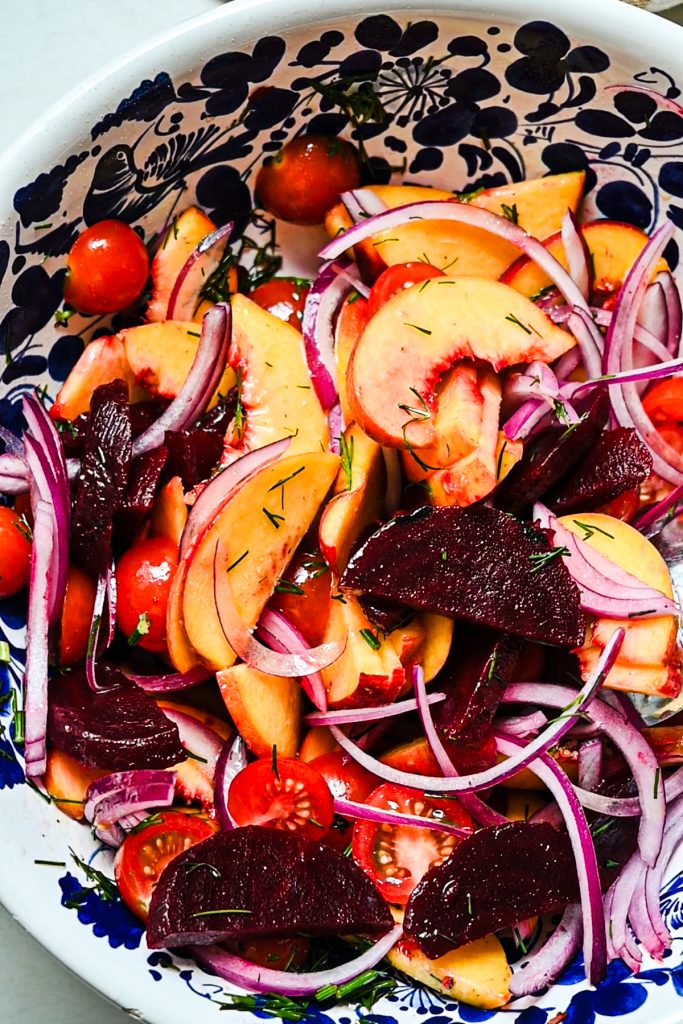 Peaches, beets, tomatoes and onions mixed with dressing in a salad bowl.