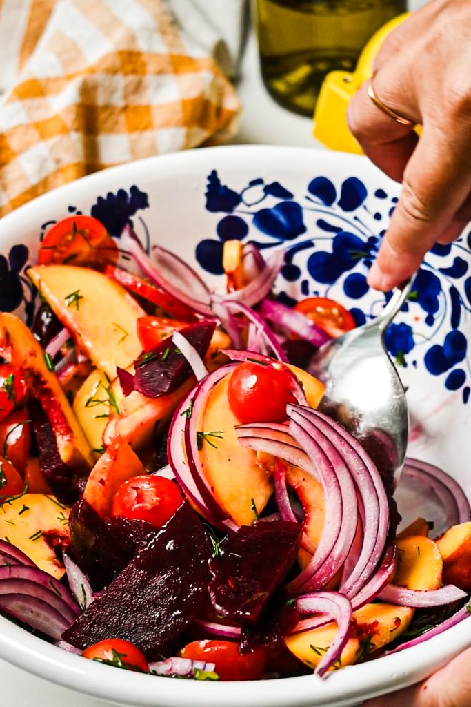 Hand using a spoon to mix the peach and beet salad together.