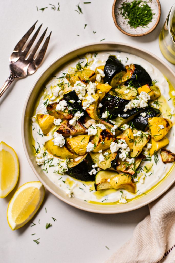 Overhead shot of a roasted zucchini and squash with yogurt dill sauce in a bowl.