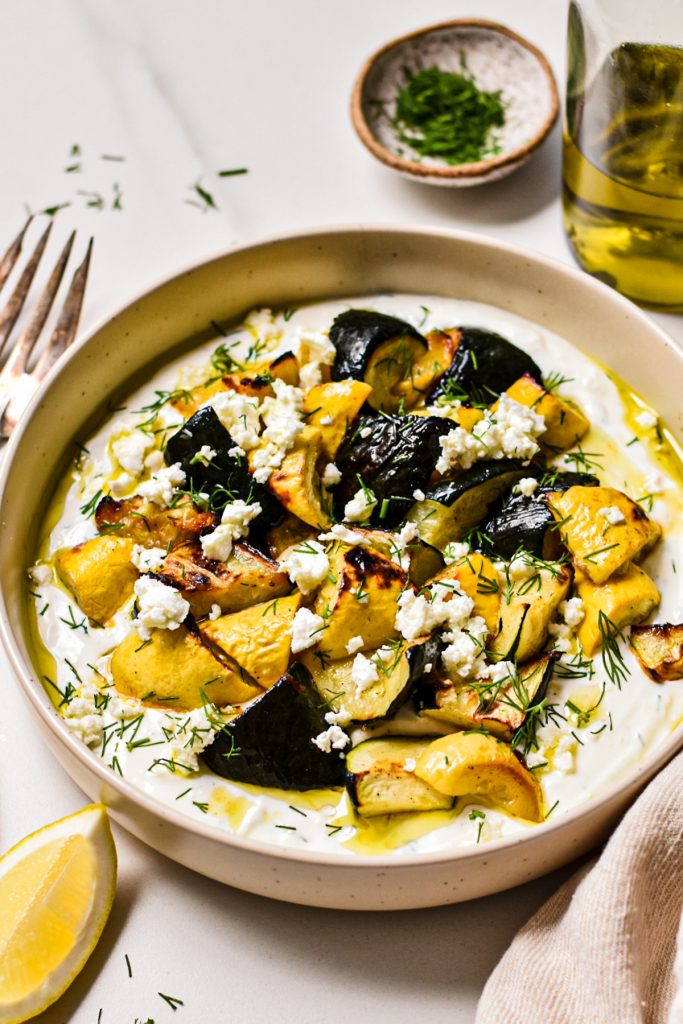 Shallow bowl with roasted zucchini and squash on a bed of dill yogurt sauce.