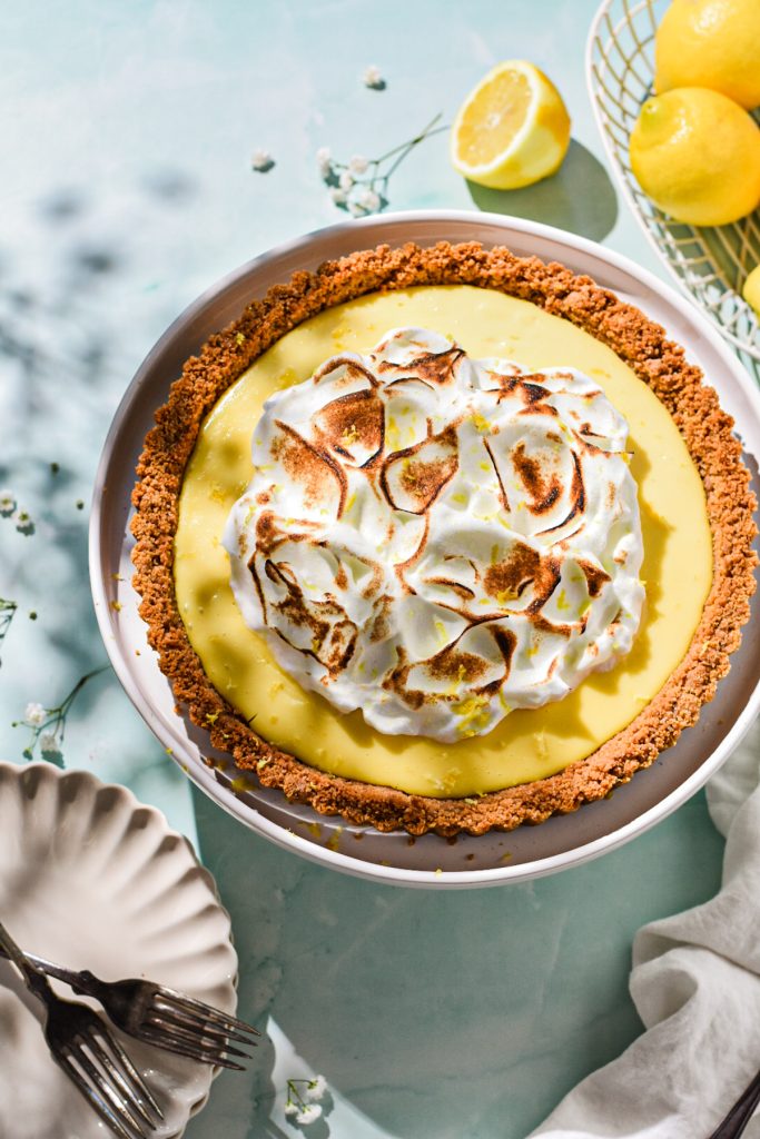 Overhead shot of lemon tart with meringue on top next to fresh lemons.