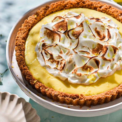 Side view of lemon tart with meringue on top on a white platter.