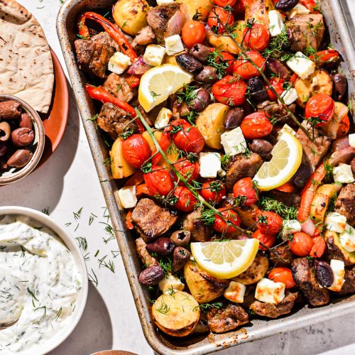 Overhead shot of sheet pan pork soulvaki on a sheet pan garnished with lemon wedges.
