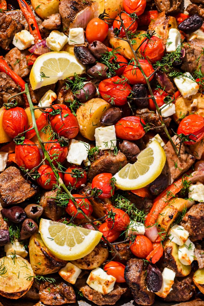 Close up of sheet pan pork souvlaki with veggies, feta, lemon and dill.