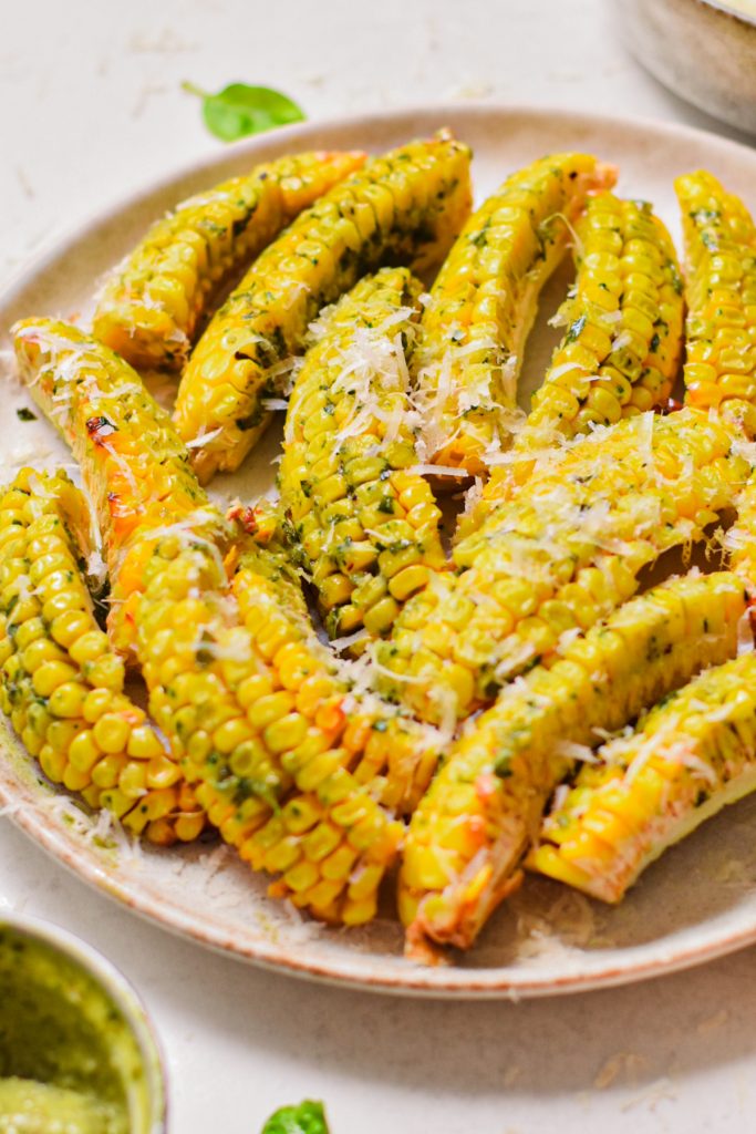 Side view of crispy corn ribs with pesto butter and parmesan on top.
