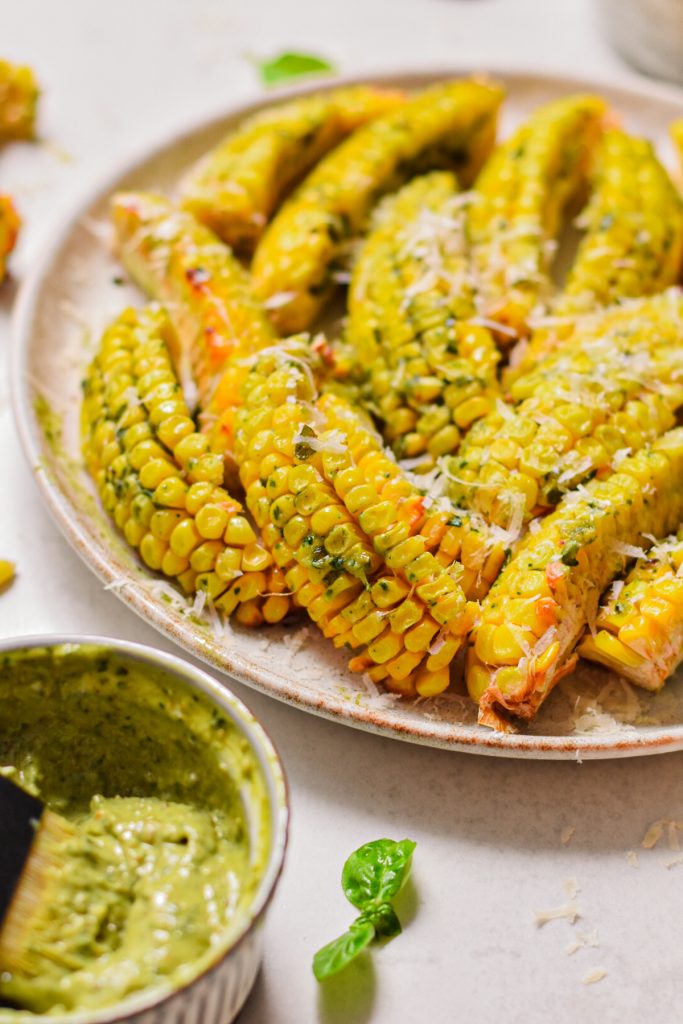 Pesto butter corn ribs with parmesan served on a plate with more pesto butter on the side.