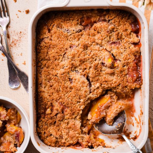 Overhead shot of peach crisp in a baking dish with a metal spoon.