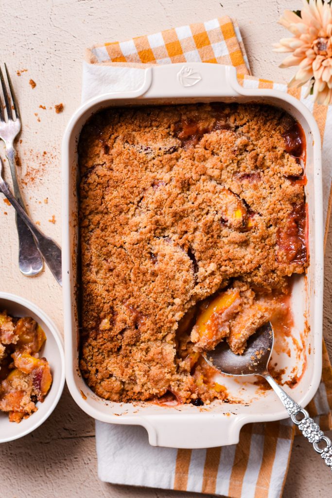 Overhead shot of peach crisp in a baking dish with a metal spoon.