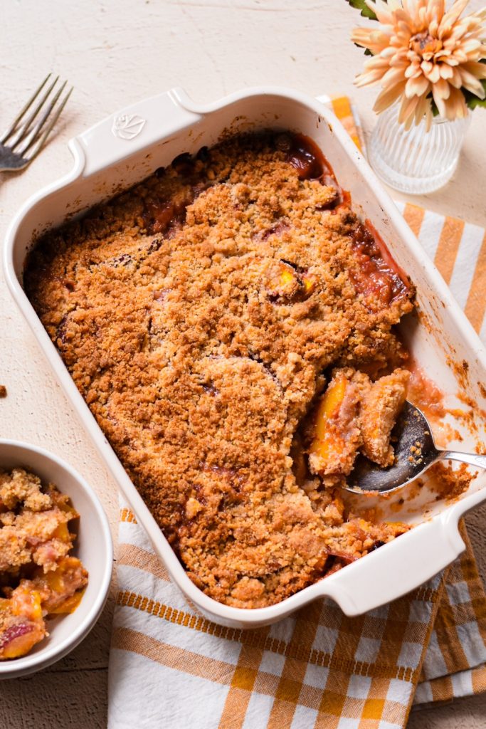 Peach crisp in a white baking dish with some placed in a bowl next to it.