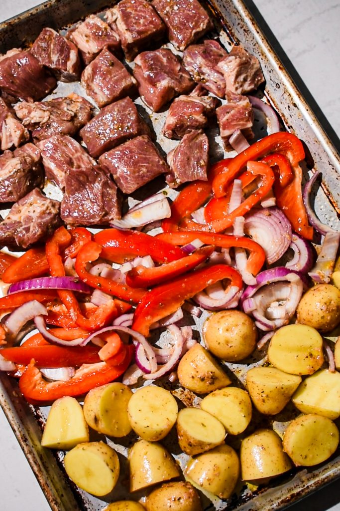 Marinated pork, chopped veggies and potatoes on a sheet pan.