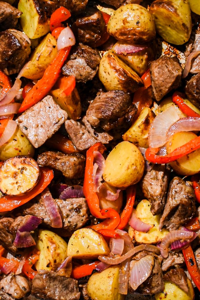 Close up of sheet pan pork souvlaki with vegetables and potatoes on a sheet pan.