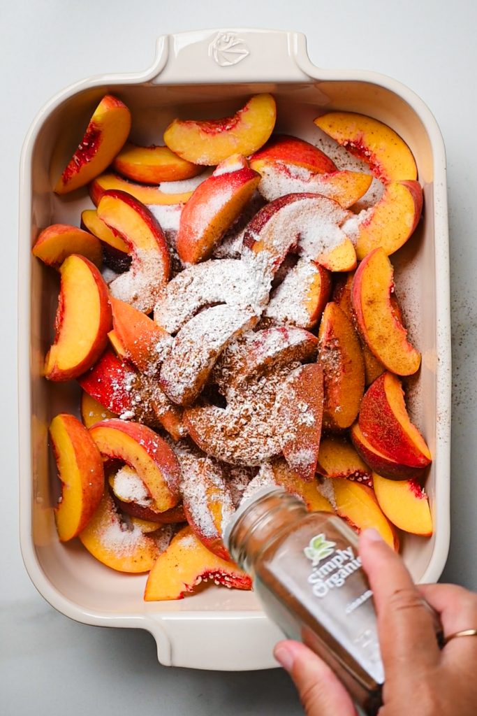 Hand sprinkling cinnamon on top of the sliced peaches.
