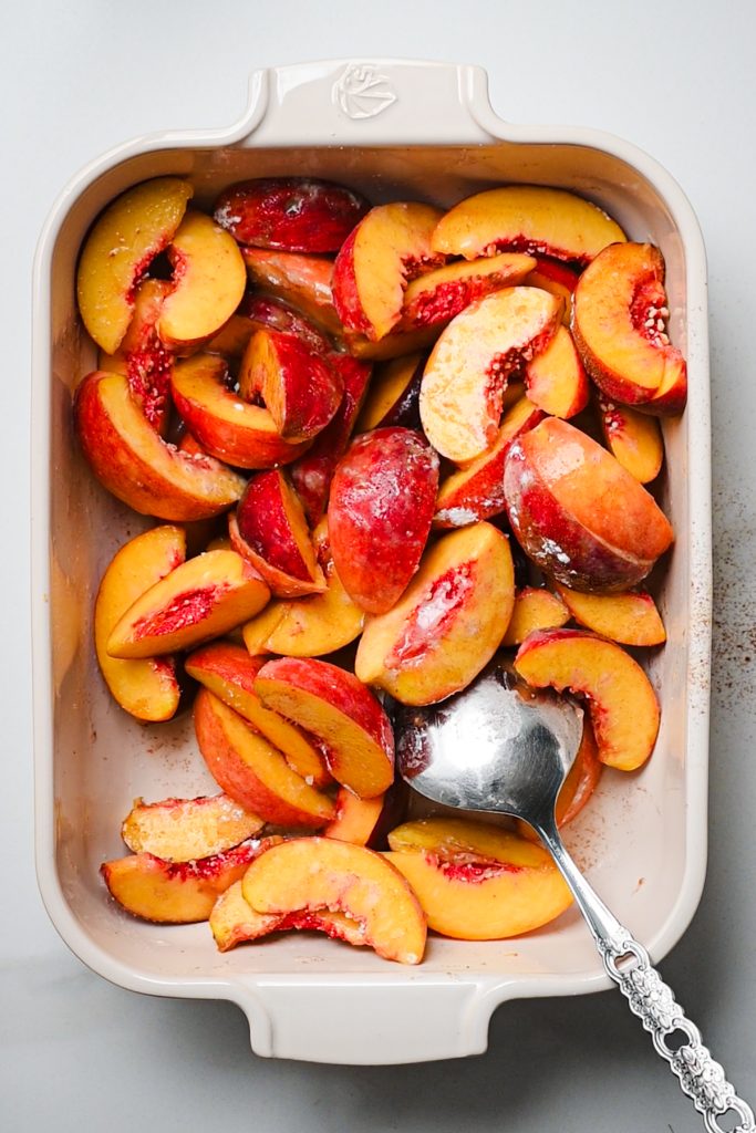 Using a metal spoon to mix the peaches with sugar and cinnamon.