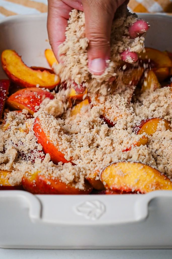 Hand sprinkling the crisp topping on top of the fresh peaches.