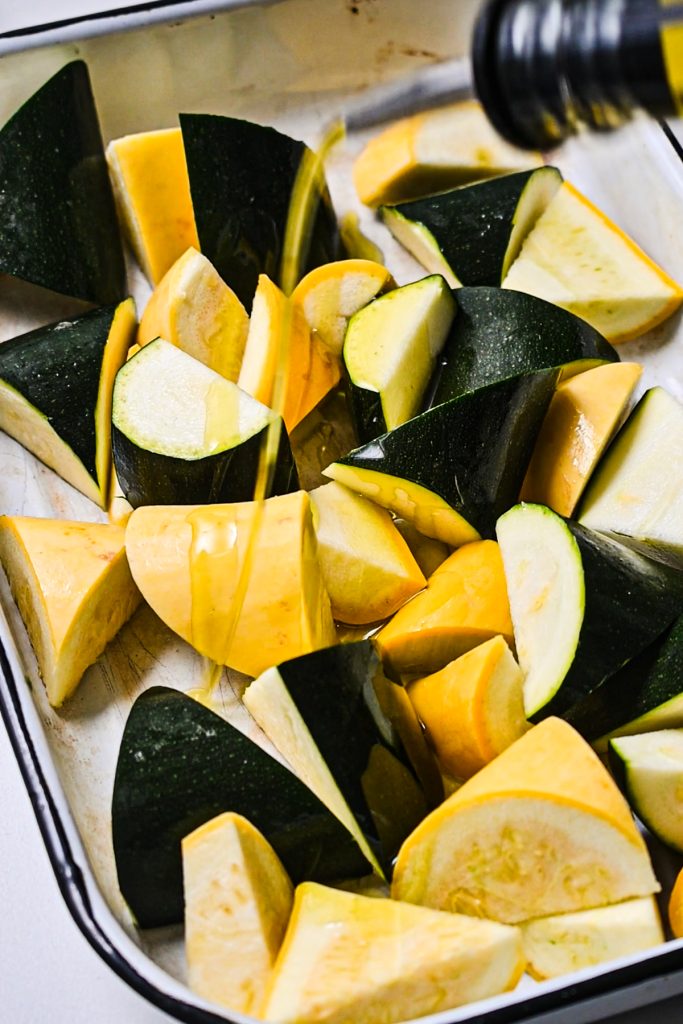 Drizzling olive oil on top of chopped zucchini and squash.
