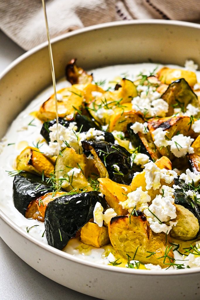 Drizzling olive oil on top of the assembled roasted zucchini and dill yogurt sauce.