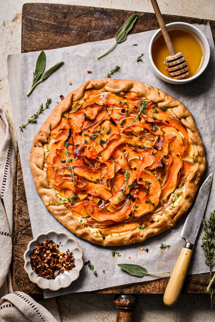 Butternut squash and goat cheese galette on parchment on a wooden board.