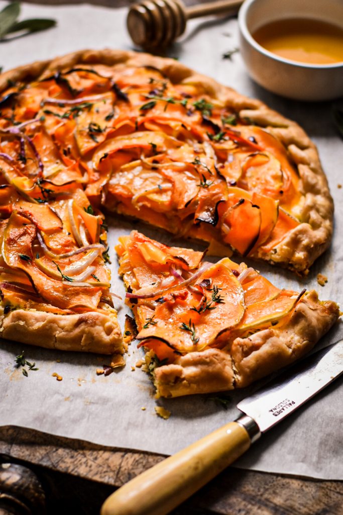 Butternut squash and goat cheese galette with one slice out of it on a wooden board.