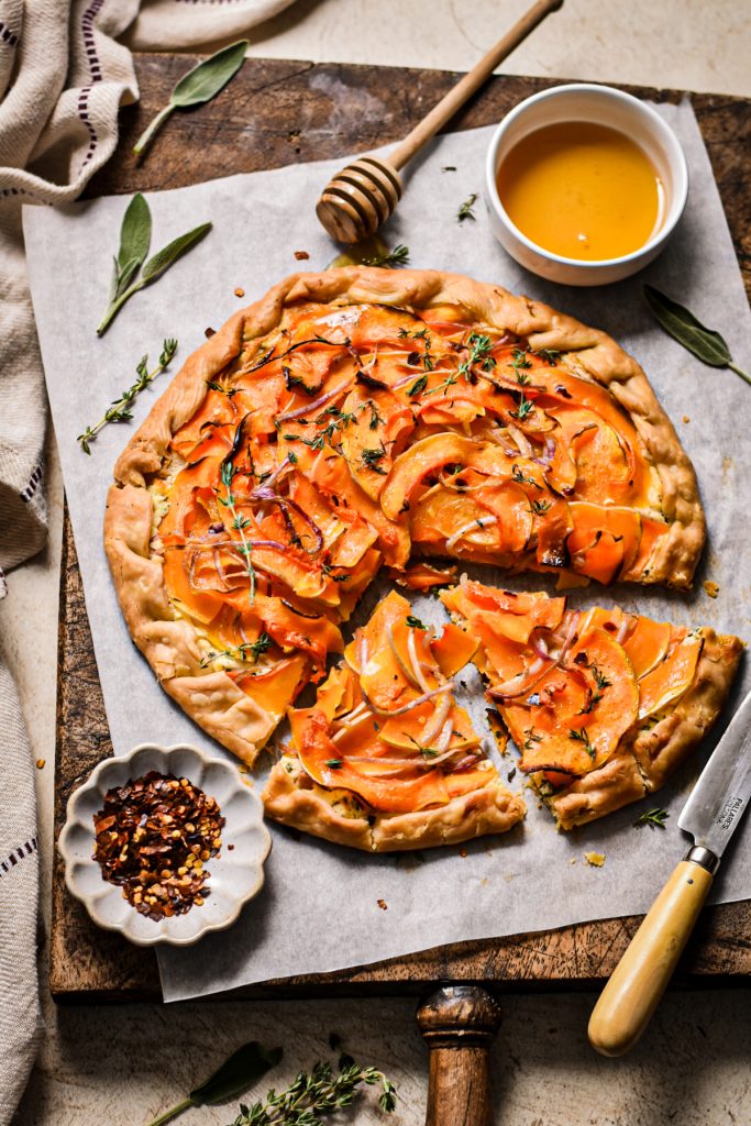 Butternut squash and goat cheese galette on a wooden board with two slices taken out.