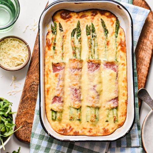 Ham and asparagus gratin with parmesan mornay sauce in a baking dish on a wooden board.