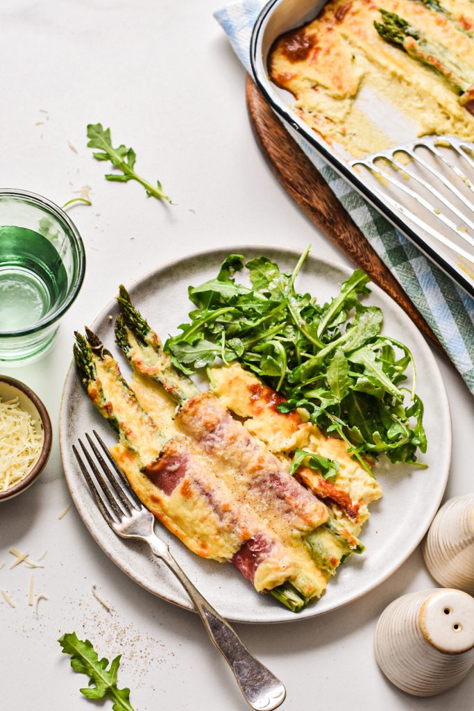 Portion of ham and asparagus mornay on a plate with a side salad.