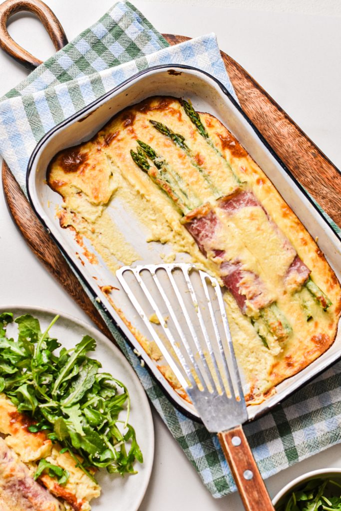 Ham and asparagus gratin in a baking dish with a spatula where some is missing.