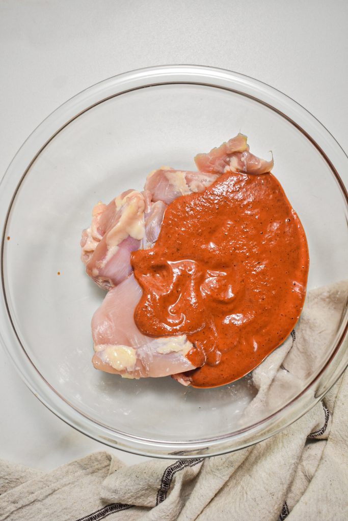 Chicken thighs in a mixing bowl with chile marinade on top.